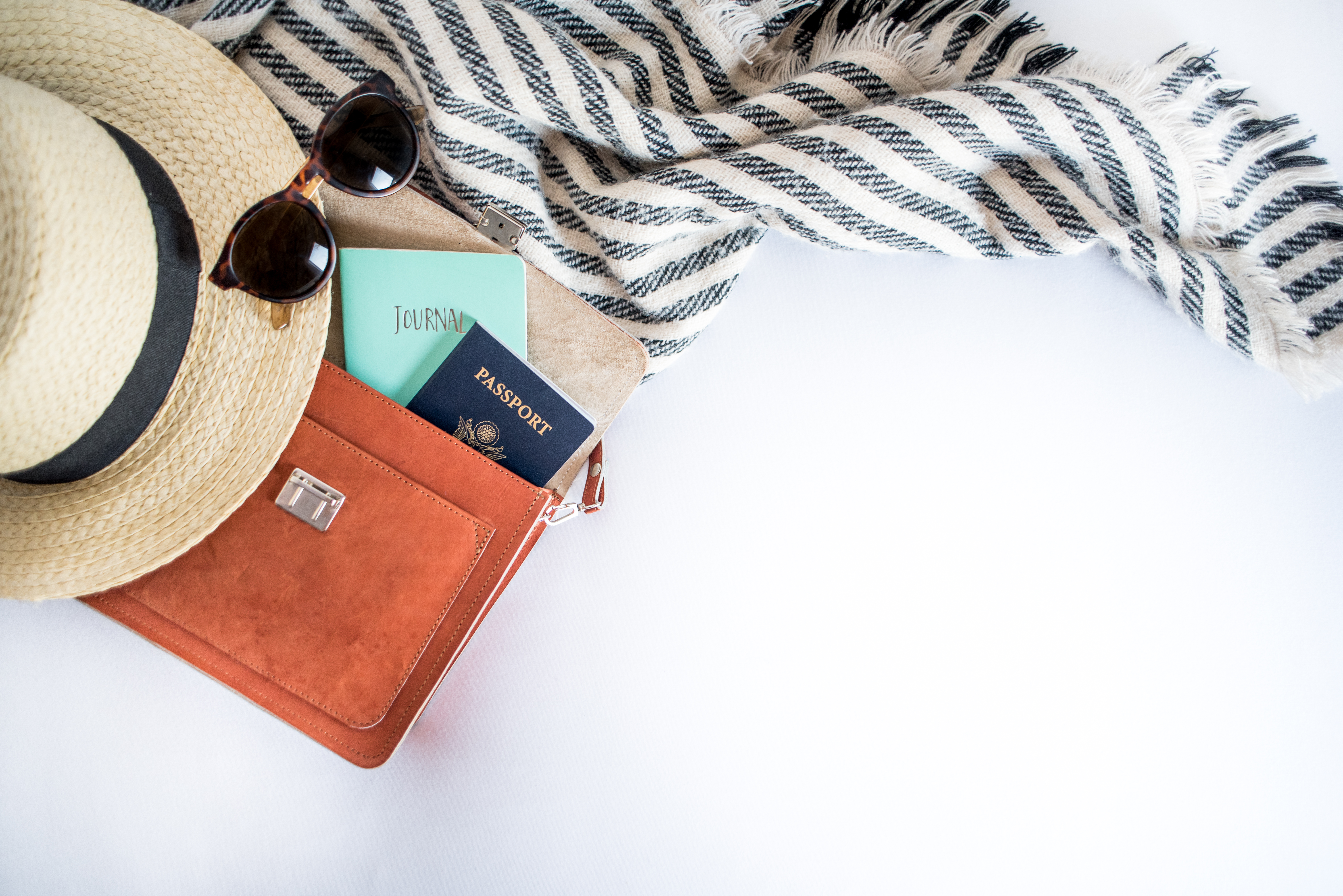 Straw sunhat, sunglasses, small leather travel bag with passport and travel documents, and a scarf.